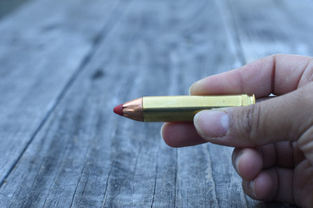 Hand holding Red tip 450 Caliber ammunition on wooden background
