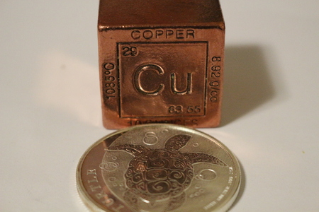 A copper cube next to a silver coinの写真素材