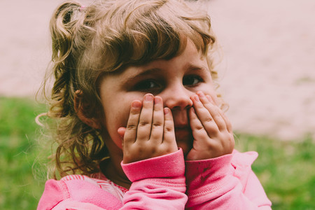 little girl in pink sweater outdoors acting shyの写真素材