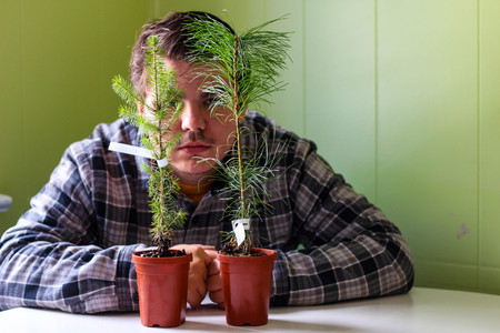 A young man aged 20 to 25 hiding behind two tiny plants that are ready to be planted. Concept of environmentalistの写真素材