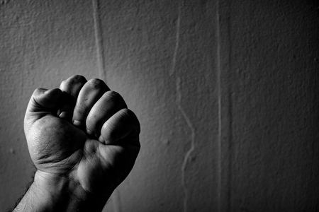 An aggressive monochrome adult male clenched fist isolated on a black background..の写真素材