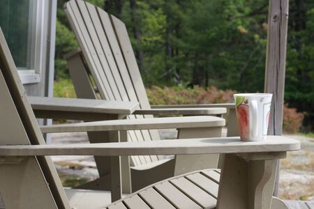 A coffee mug sitting on a Muskoka chair on a dock. Lake and cottages in the background - horizontal orientation. Perfect for cottage related material.の写真素材