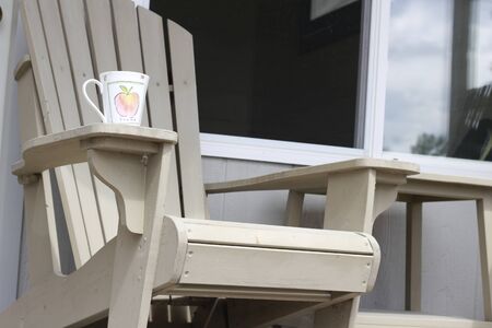 A coffee mug sitting on a Muskoka chair on a dock. Lake and cottages in the background - horizontal orientation. Perfect for cottage related material.の写真素材