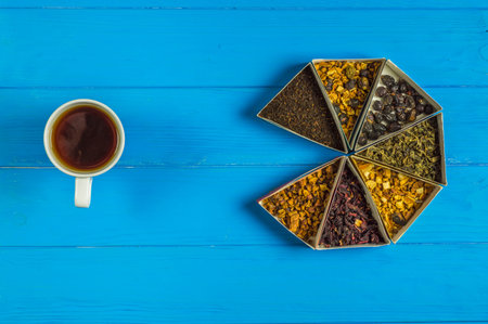 Face reflected in tea cup next to dry tea set on blue table