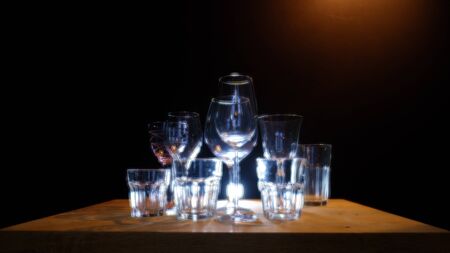 Close ups of wine-, long drink- and spirits-glasses on a wooden shelve in a bar, in front of a dark background, illuminated by colorful spot lights, creating blurry light effects with beautiful  bokehの写真素材