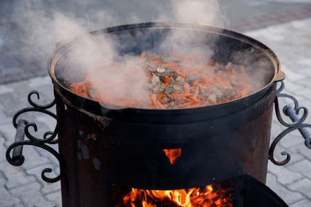 meat for pilaf with large pieces of carrots is cooked in a cauldron on the fireの写真素材