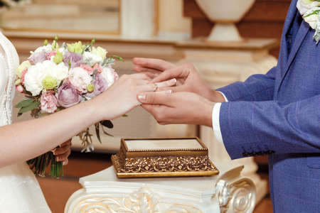 the groom in a dark blue suit carefully puts the ring on the bride's hand on the ring fingerの写真素材