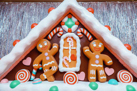 gingerbread men under the roof of a gingerbread house decorated with Christmas candies and snowの写真素材