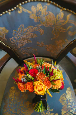 a bouquet of orange roses and alstormeria stands on a dark green chair trimmed with golden leavesの写真素材