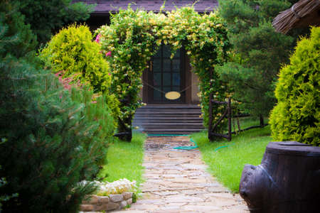 Backyard garden with sidewalk path and trimmed bushes, green grass and houseの写真素材