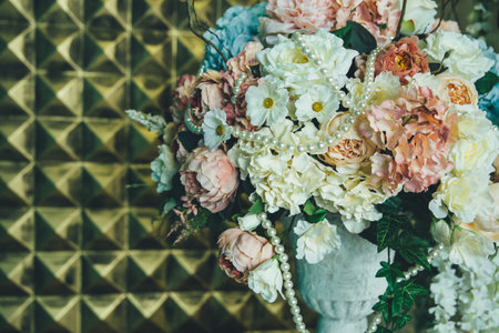 flower arrangement of artificial roses, peonies and hydrangeas, decorated with artificial pearls, against a background of golden panels on the wallの写真素材