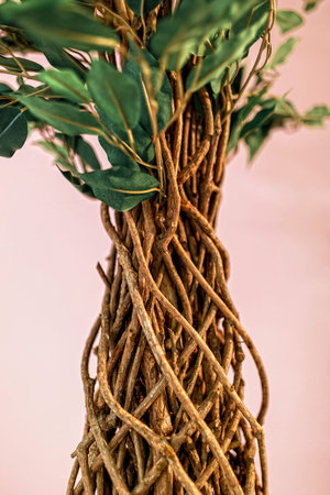part of an artificial tree made of wicker branches and fabric leaves on a pink background