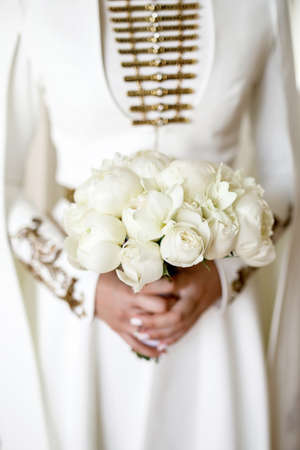 a girl in a wedding national Caucasian dress holds a wedding bouquet of white peoniesの写真素材