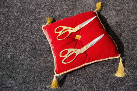 2 pairs of ribbon cutting scissors lying on a red velvet pillow on a dark gray backgroundの写真素材