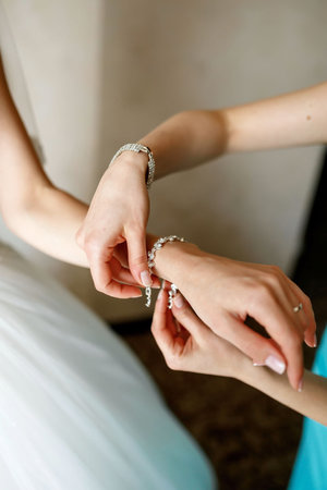 bridesmaid puts on a girl an elegant bracelet on her hand on the background of the room and wedding...