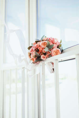 a bouquet of pink peonies and roses, decorated with eucalyptus leaves and a white ribbon against the background of a window and sunlightの写真素材