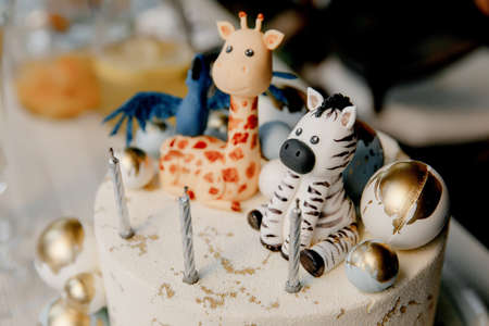 birthday cake decorated with animal figurines, zebra and giraffe, candles and golden balloonsの写真素材