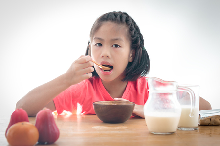 cute little Asian girl eating cereal with the milk on white backgroundの写真素材