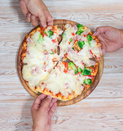 Friends hands taking slices of pizza. Top view on woodの写真素材