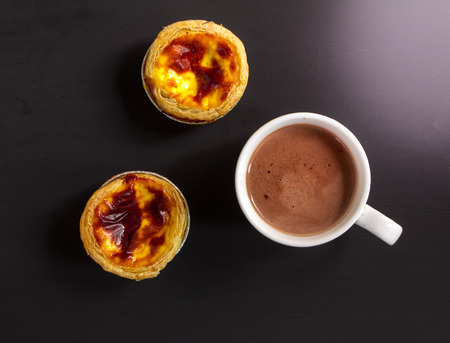 Hot chocolate in white cup with egg tart on black background, Top viewの写真素材