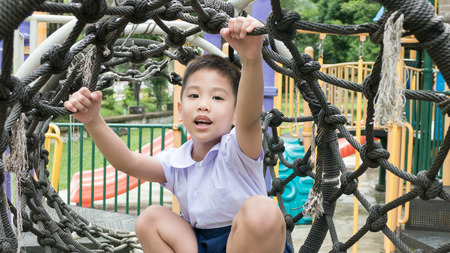 Thai school boy in uniform play alone at the rope net in the play ground.の写真素材