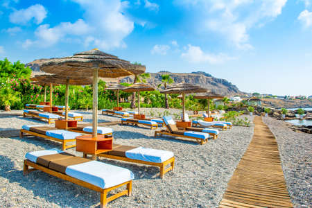 Beautiful rocky beach with sunbeds and straw umbrellas on the shore of Mediterranean Sea in Rhodes island, Greeceの写真素材