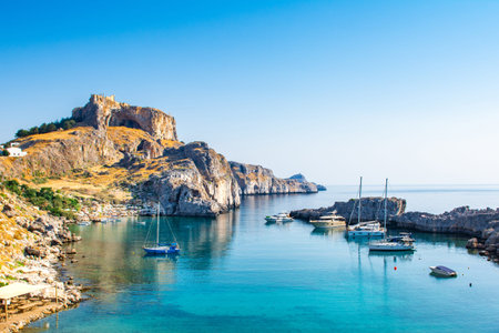 Rhodes, Greece - 14 August 2019: Sunset landscape of beautiful St. Paul's Bay in Rhodes island with mountain, rocky beach and yacht marinaのeditorial素材