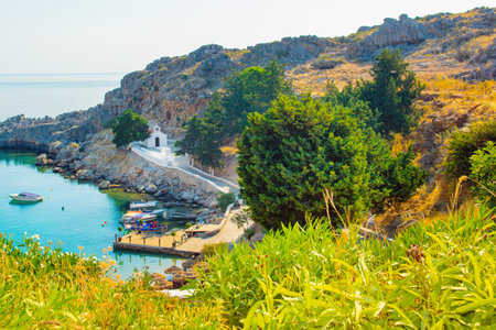 Rhodes, Greece - 14 August 2019: Sunset landscape of beautiful St. Paul's Bay in Rhodes island with mountain, rocky beach and yacht marinaのeditorial素材