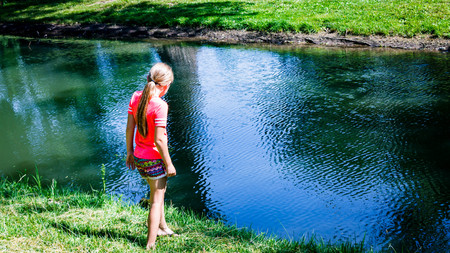Little girl looking at fish in a small pondの写真素材