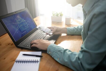 A man using a smart phone and notebook computer commands electronic appliances in his home. man at his workplace using technology, flare lightの写真素材