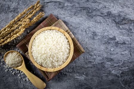 Japanese rice in a wooden cup, placed on a cloth and a wooden spoon and all the ears in the stone. Top view.の写真素材