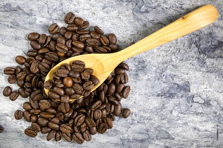 Roasted coffee beans in a wooden spoon placed on a pile of coffee beans on a stone plate. Top view.の写真素材