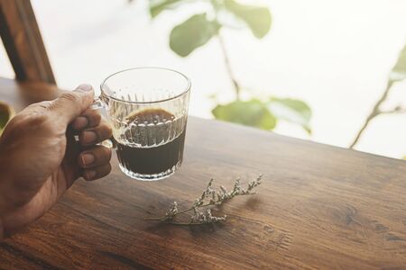 Close-up of male hand holding coffee at early morning in cafe, flare light. with vintage tone.の写真素材