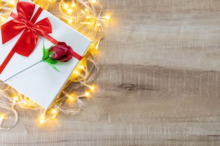 Gift box with beautiful red ribbon, rose and decorative lights, concept of Valentine's, anniversary, mother's day and birthday greeting, copyspace, topview. wooden background.の写真素材