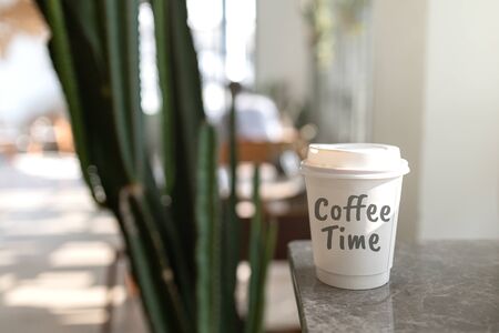 White paper cup on Marble table in coffee shop. with text Coffee time. Blurred coffee shop background.の写真素材