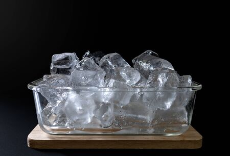 Ice in a glass bowl put on a wooden tray on black background.の写真素材