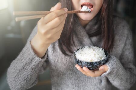 Asian women holding cooked jasmine rice bowls with chopsticks. Wearing a gray sweater.の写真素材