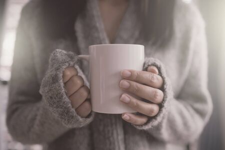 The girl holding the mug of hot coffee in her tender hand. in the morning soft sunlight.の写真素材