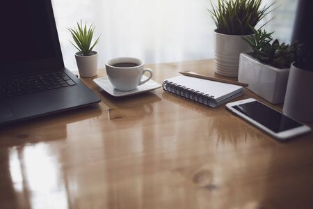 Home office in the morning with sunlight from window. with laptop, white coffee cup, notebook and smart phone on working desk table.の写真素材
