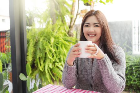 Asian woman relaxing on table with hot coffee at the garden in the house.の写真素材
