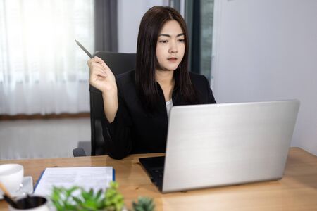 Asian woman working Holding a pen in home with laptop computer smile and happy work. Work from home concept.の写真素材