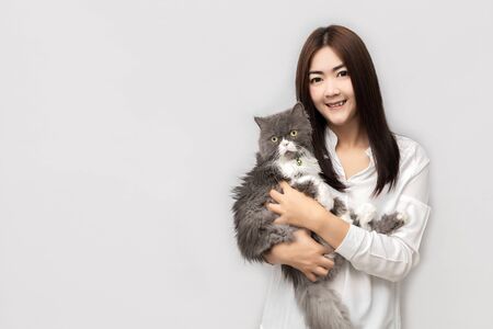 Asian woman with long hair wearing a white shirt is carrying a grey Persia Cat.の写真素材