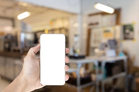 Mockup image of hand holding white mobile phone with blank white screen, blurred cafe background.の写真素材