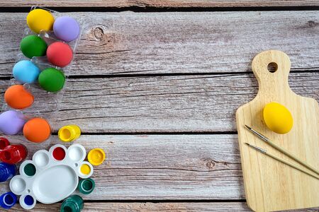 Pile of painted ester eggs in various colors and with brush and paint on wooden table. Ester holiday concept.の写真素材