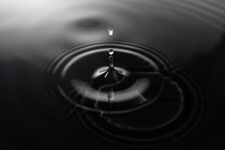 Close-up of a water drop impact on black background with water surface, causing rings on the surface.の写真素材