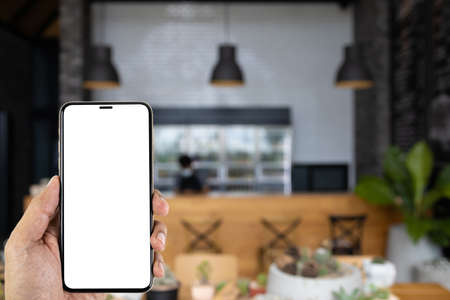 A man hand holding smart phone device in the blur coffee shop or blur cafe background.の写真素材
