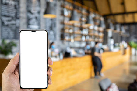 A man hand holding smart phone device in the blur coffee shop or blur cafe background.の写真素材