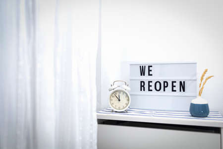 Words WE REOPEN and reopening on the light box and vintage alarm clock. New life, new business, new deals concept.の写真素材