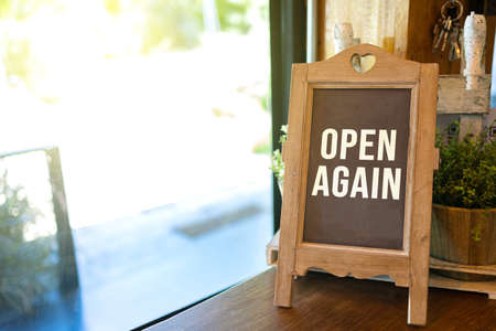 Vintage blackboard with text OPEN AGAIN on wooden table by the window. Reopen business concept.の写真素材