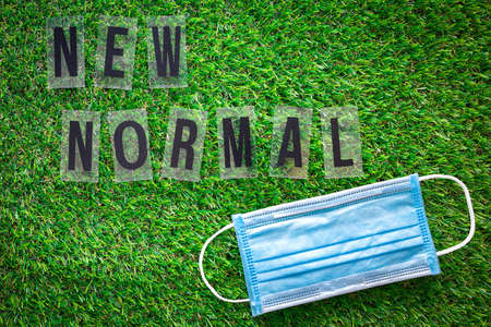 Blue sanitary mask and NEW NORMAL letter on green grass. New normal concept.の写真素材